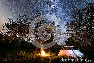 Night camping. tourist tent near campfire under trees and beautiful starry sky and milky way Stock Photo