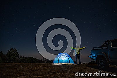 Night camping. Man hikers stands and raise both arms up from enjoying the beautiful night sky with stars. Male trekkers relaxing Stock Photo