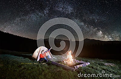 Couple tourists near campfire and tents under night sky full of stars and milky way Stock Photo