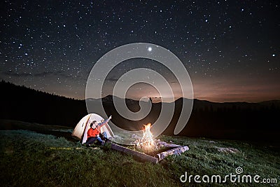 Tourists near campfire and tent under night starry sky Stock Photo
