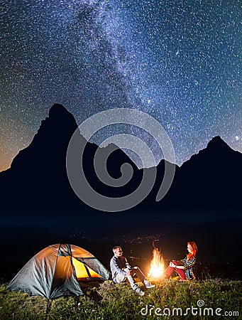 Night camping. Romantic pair sitting near campfire and tent under incredibly beautiful starry sky and Milky way Stock Photo