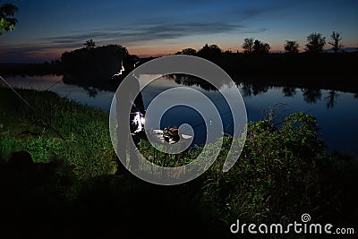 Night fishing, fisherman with a fishing rod standing on the shore of lake Stock Photo