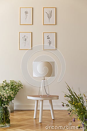 A night lamp on a stool surrounded by bunches of wild flowers against a vanilla wall with nature drawings in a wooden floor room i Stock Photo