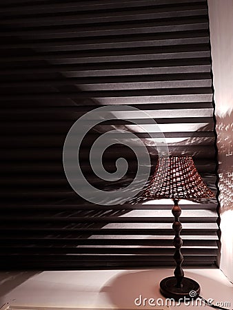 night lamp on a white windowsill against a background of black blinds, conceptual Reflection Stock Photo