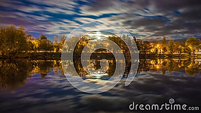 Night landscape above river with trees lit by city lights and clouds in motion Stock Photo