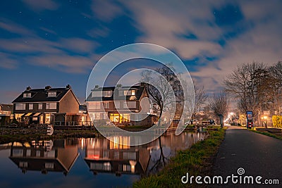 Night landscape with starry sky in the Dutch village of Streefkerk. Houses with bright light reflecting in the shine of the water Stock Photo