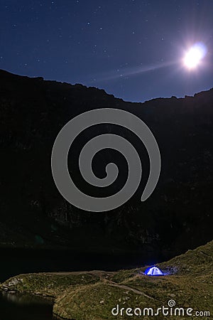 Night mountain landscape with illuminated blue tent. Mountain peaks and the moon. outdoor at Lacul Balea Lake, Transfagarasan, Stock Photo