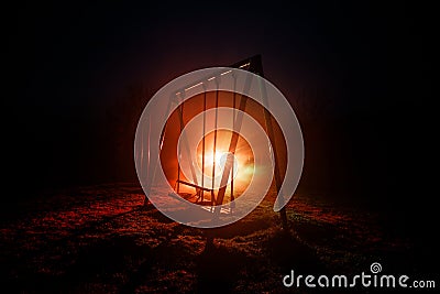 Night photo of metal swing standing outdoor at night time with fog and surreal toned light on background. Nobody there. Stock Photo