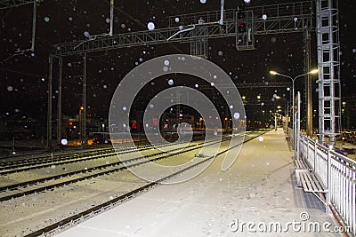 Night railway station. Snowfall. The lights of the city in the background. Stock Photo
