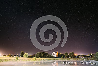 Night Sky Stars Over River Lake Near Houses In Village. Night Starry Sky Above Rural Landscape In Belarus. Glowing Stars Stock Photo