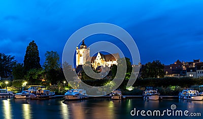 Nightime view of the illuminated Notre Dame catholic church in Dole with houseboats on the Doubs River in the foreground Editorial Stock Photo