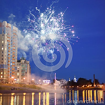 Nightly fireworks near river and city lights reflecting in water Stock Photo