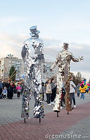 NIKOPOL, UKRAINE - 09/28/2021: Close-up of stilt walkers at the fair. Male acrobats dressed in shiny mirrored costumes. The Editorial Stock Photo