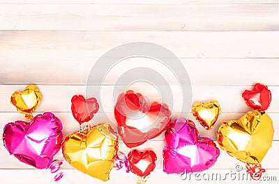 nine shiny pink red and golden heart-shaped balloons with ribbons on a beige and white wooden background. Valentine&#s Stock Photo