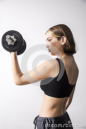 A nineteen-year-old smiling girl with a bob hairstyle and bleached strands in a gray short top holds a dumbbell Stock Photo