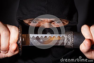 Ninja ready to fight, holding a Japanese sword. Photo of a warrior dressed in black clothes and closed face Stock Photo