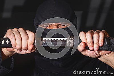 Ninja ready to fight, holding a Japanese sword. Photo of a warrior dressed in black clothes and closed face Stock Photo