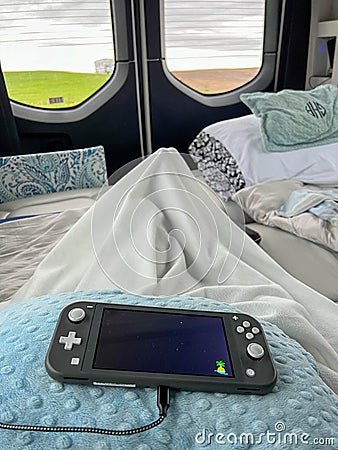 A Nintendo Switch on a persons lap while relaxing in a camper van looking toward the back window Editorial Stock Photo