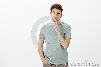 No one should no, keep mouth shut. Portrait of charming confident european man in t-shirt, saying shh while showing Stock Photo