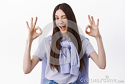 No problem, excellent. Brunette girl winking and showing okay gesture, OK sign, like and approve, assure everything good Stock Photo