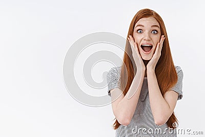 No way awesome. Charming ginger girl screaming enthusiastic thrilled open mouth widen eyes surprised touch cheeks Stock Photo