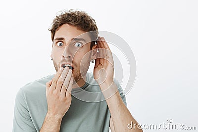 No way, tell me everything. Portrait of shocked and amazed handsome guy with fair hair, dropping jaw, covering opened Stock Photo