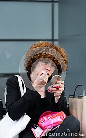 non-binary person applies lipstick sitting on a bench Stock Photo