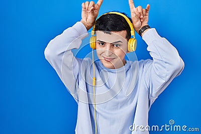 Non binary person listening to music using headphones doing funny gesture with finger over head as bull horns Stock Photo