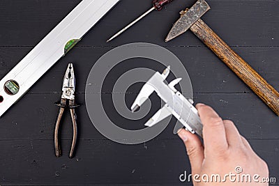 Nonius hand tool in the hand above black wooden table board with old used hand tools. Top view of old used tools on the table. DIY Stock Photo