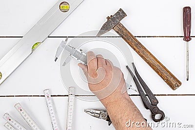 Nonius hand tool in the hand above white wooden table with old used hand tools. Top view of old used hand tools on the table Stock Photo