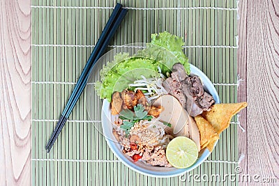 Noodle with tom yam topped with minced pork,chicken liver,wonton,shrimp ,chili. and green lemon on green. Stock Photo