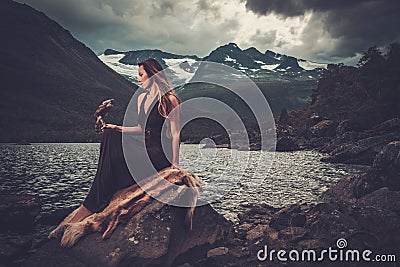 Nordic goddess in ritual garment with hawk near wild mountain lake in Innerdalen valley. Stock Photo