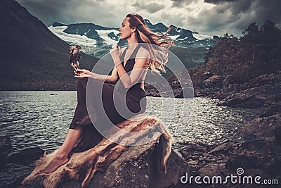 Nordic goddess in ritual garment with hawk near wild mountain lake in Innerdalen valley. Stock Photo