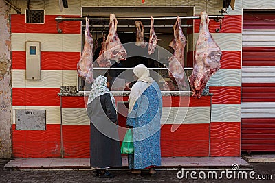 Morocco. Taroudant. Two women in traditional dress in front of a storefront of a butcher's shop Editorial Stock Photo
