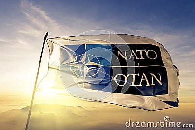 North Atlantic Treaty Organization NATO OTAN logo. flag textile cloth fabric waving on the top sunrise mist fog Editorial Stock Photo