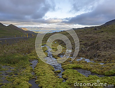 Northern summer landscape with green moss and water puddles, asfalt road curve, grass, rock, colorful mountains and dramatic Stock Photo