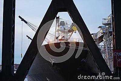 Nose deck big black cargo ship anchored at discharge for download through triangular truss metal bridge view Stock Photo