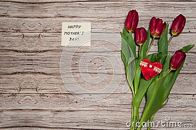 A note wishing you a happy mother`s Day and a spring bouquet of red tulips on a wooden background. Stock Photo