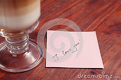 A note with the words `I love you` and a Cup of cappuccino on a wooden table Stock Photo