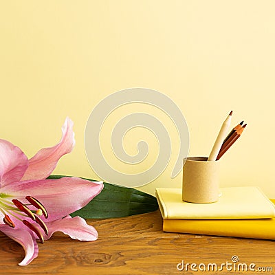 Notebook, colored pencils, flower on wooden desk. Yellow background Stock Photo