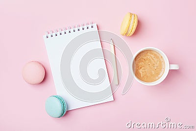 Notebook, cup of coffee and colorful macaron on pastel pink desk top view. Cozy morning breakfast. Fashion flat lay. Stock Photo