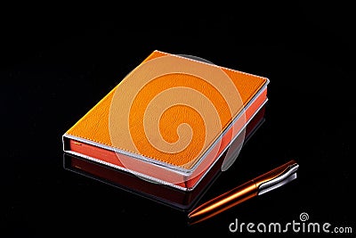 Notebook and pen bright orange on a black background. Stock Photo