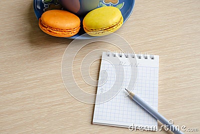 Notebook with pencil, list of plans. Macaroons next to a notebook on a wooden table Stock Photo