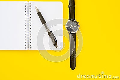 Notebook with ring binder with penand a wristwatch with leather straps, isolated on a yellow backdrop with copy space. Concept of Stock Photo