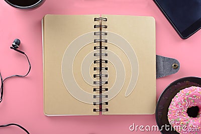 A notebook on springs with brown pages rests on a pink background. Around the notepad there are coffees donuts and a Stock Photo