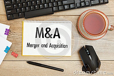 Notebook with text - M and A Merger and Acquisition, keyboard and a cup of tea Stock Photo