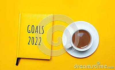 Notebook with the words Goals 2022 and a cup of coffee on a yellow background. Motivation, inspiration. Planning, plans and tasks Stock Photo