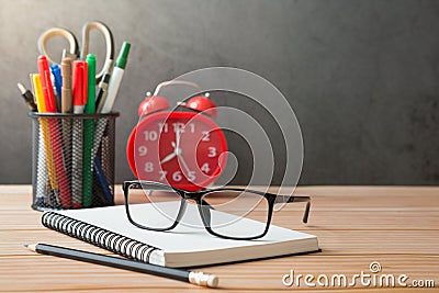 Notebooks, pens, pencil holder, glasses, Red alarm clock on wooden desks and loft walls with sunlight and copy space Stock Photo