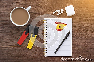 Notepad with spanish flag, wireless headphones, coffee cup, pen, markers on brown table Stock Photo