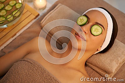 Nothing better than a facial to unwind. A beautiful young woman lying on a massage table at the spa with cucumer over Stock Photo